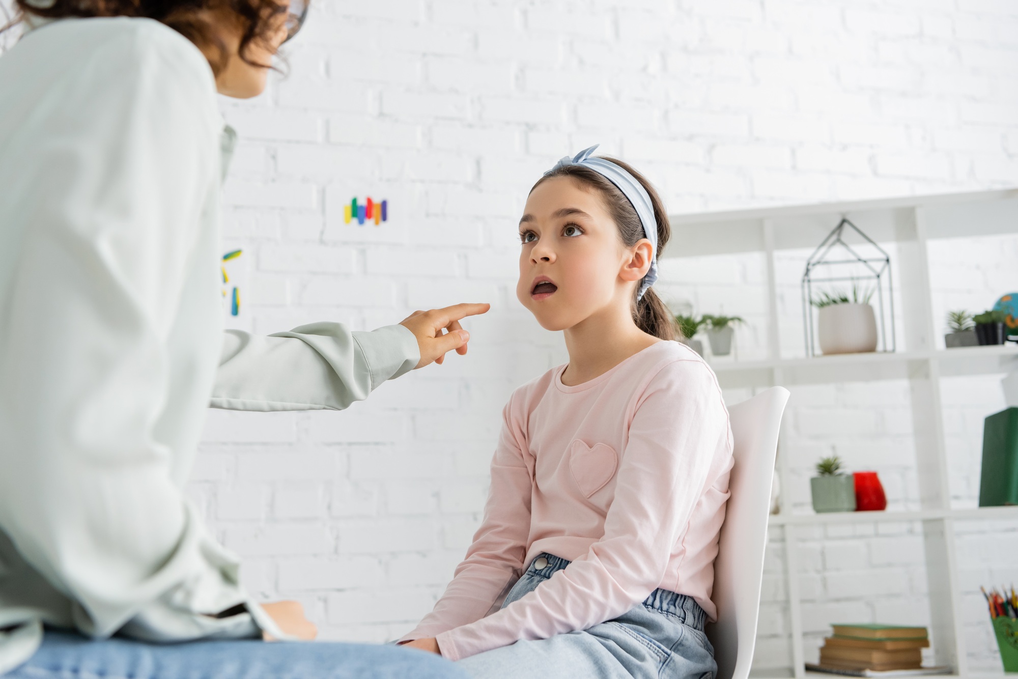Speech therapist pointing at cheek of preteen girl in consulting room